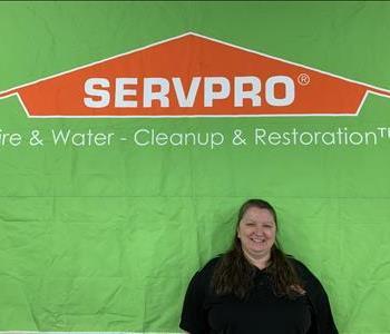 white woman in grey sweater with green shirt standing in front of green SERVPRO van