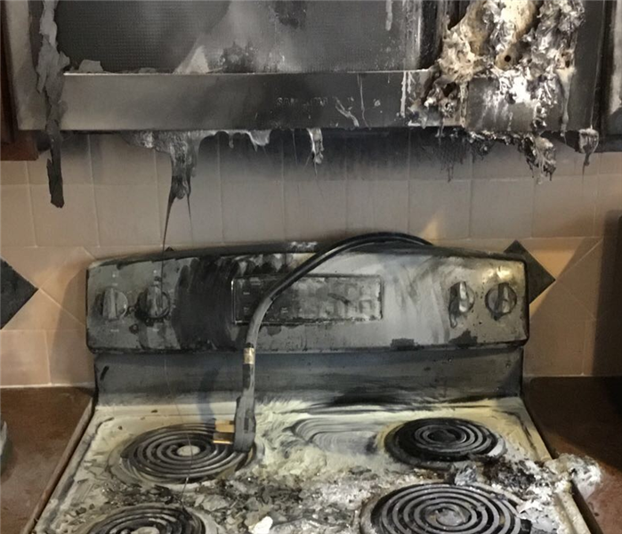 Black stove that caught fire and melted the microwave that was mounted above it.