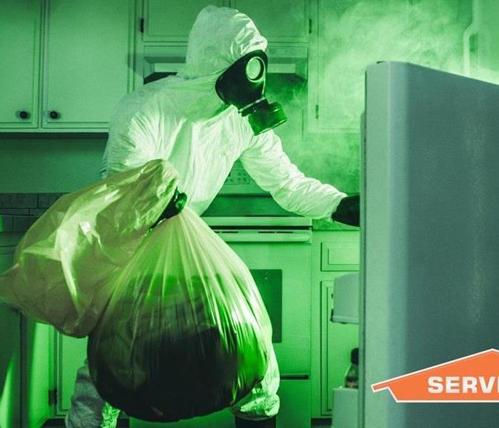 A SERVPRO tech holding a trash bag and opening a refrigerator